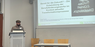 Christoph Burzlaff steht an einen Podium vor einer Präsentation, die an der Wand projiziert wird. Der Titel der Präsentation wird abgebildet: "Bereit für die Zukunft? - Die Entwicklung der Berufsförderungswerke im Kontext aktueller Transformationsprozesse."