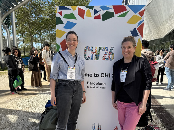 Zu sehen sind Jana-Sophie Effert und Frauke Mörike vor einem Schild der CHI 26 in Barcelona